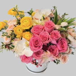 Pink and yellow roses arranged in a white vase with white orchids