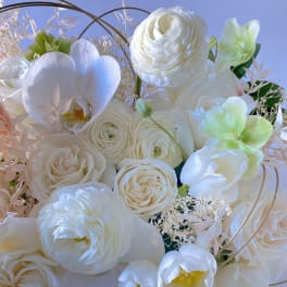 White bouquet with roses, ranunculus, and orchids against a blue background