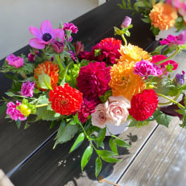 Bright mixed bouquet with dahlias, roses, and pink anemone in a white container