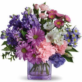 Pastel bouquet of purple and pink blooms with white accents in a lavender glass cube vase