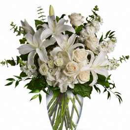 White lilies, roses, and hydrangeas arranged in a clear glass vase with visible stems.