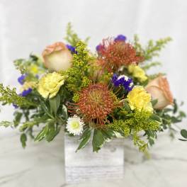 Mixed floral arrangement in a white square vase with peach roses and yellow blooms