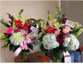 Two tall mixed flower arrangements with hydrangeas, pink roses, lilies, and red gerbera daisies in glass vases.