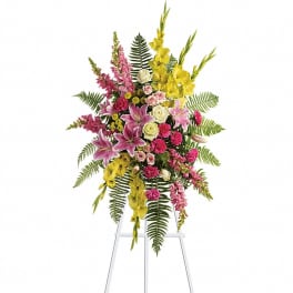 Tall standing spray of pink lilies, roses, and yellow flowers on a white easel.