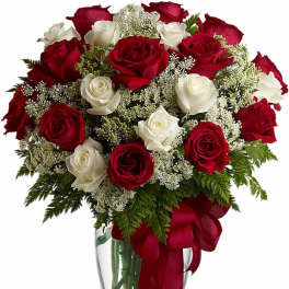 Arrangement of red and white roses with white filler flowers in a clear glass vase with red bow
