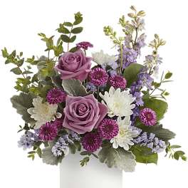 Arrangement of lavender roses, purple and white mums, and lilac blooms in a white cylinder vase