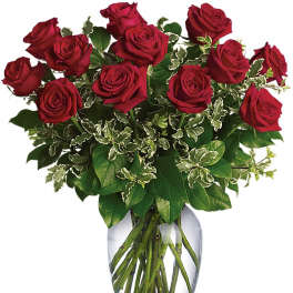 Arrangement of long-stem red roses with variegated foliage in a clear glass vase