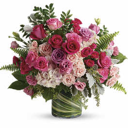 Pink and lavender rose arrangement with hydrangeas in a glass vase lined with green leaves