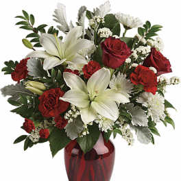 Red roses, red carnations, white lilies, and white mums arranged in a red glass vase.