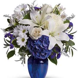 Blue and white flower arrangement with lilies, hydrangea, daisies, and roses in a blue glass vase