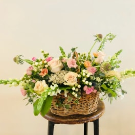 Basket arrangement of pale roses and pink flowers with greenery