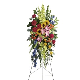 Tall standing spray of multicolored roses, lilies, sunflowers, delphinium and bells of Ireland on a metal easel