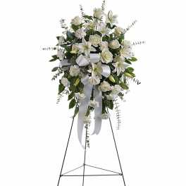 Standing spray of white lilies, roses, and carnations with a white ribbon on a metal easel.