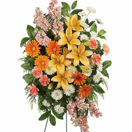 Tall standing spray with yellow lilies, orange gerberas, white mums, and pink carnations on a metal easel.