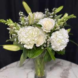 White roses and hydrangeas in a glass vase with lily buds