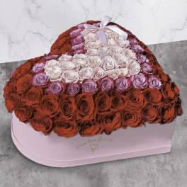 Heart-shaped boxed arrangement of red, pink, and lavender roses with a smaller pale heart and ribbon on top