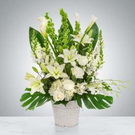 Tall white arrangement of lilies, roses, hydrangeas and calla lilies in a white woven basket