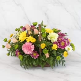 Mixed bouquet in a wicker basket with pink, yellow, white, and purple flowers