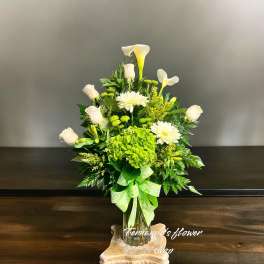 Tall white and green flower arrangement with roses, calla lilies, and hydrangea in a glass vase