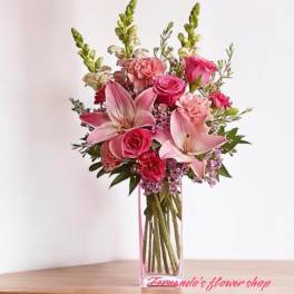 Tall pink arrangement with lilies, roses, and carnations in a clear rectangular glass vase