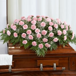 Pink carnation casket spray with white filler flowers on a wooden casket