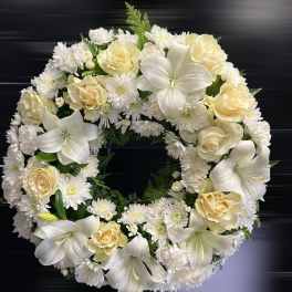 Round wreath of white lilies, cream roses, and white chrysanthemums on a dark background