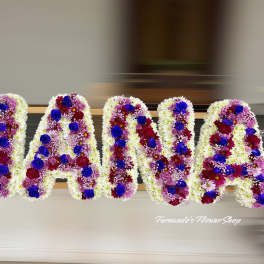 Funeral tribute letters spelling NANA in white flowers with purple and blue accents.