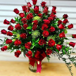 Large fan-shaped arrangement of red roses in a clear glass vase with a red bow.