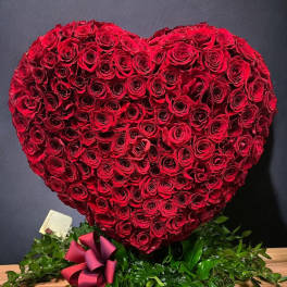Heart-shaped arrangement of tightly packed red roses with a red ribbon bow at the base