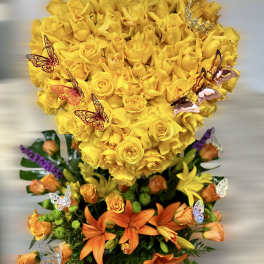 Tall arrangement with a yellow rose heart over orange lilies and roses with butterfly accents