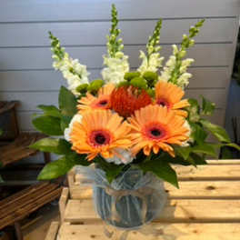 Orange gerbera daisies and white snapdragons in a glass vase