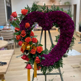 Heart-shaped floral wreath with purple blooms and orange roses on an easel