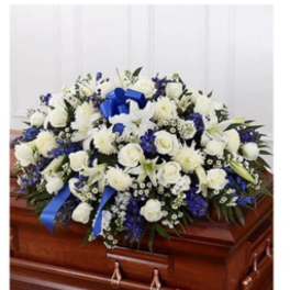 White and blue floral casket spray with ribbon on a wooden casket
