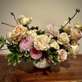 Low arrangement of cream roses, pink mums, and ranunculus in a white ceramic bowl