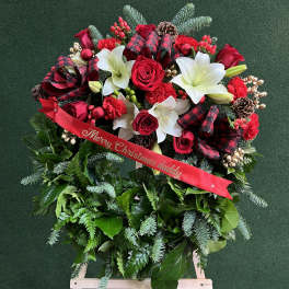 Christmas floral wreath with red roses, white lilies, and a ribbon on an easel