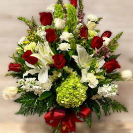 Tall red and white arrangement with roses, lilies, and green hydrangea in a glass vase with red bow.