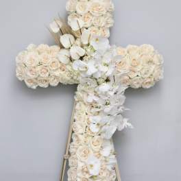 Cross-shaped floral arrangement of cream roses and white orchids on an easel