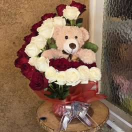 Red and white roses arranged with a teddy bear and ribbon