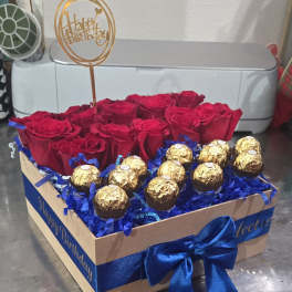 Red roses and gold-wrapped chocolates in a gift box with a birthday topper
