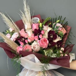 Bouquet of pink and burgundy roses with pampas grass and white wrap