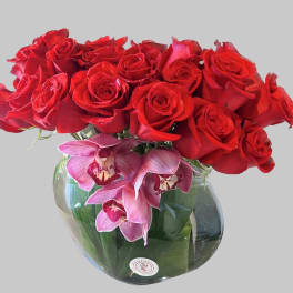 Red roses and pink orchids arranged in a round glass vase.