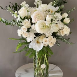 White roses and orchids arranged in a tall glass vase