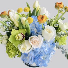 Bouquet of white roses, blue hydrangeas, and orange ranunculus in a vase