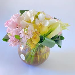 Pink roses and orchids arranged in a round glass vase