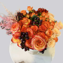 Bouquet of orange and cream roses with dark berries in a white vase