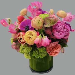 Bright mixed bouquet in a green glass vase with pink and peach blooms