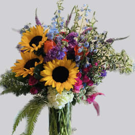 Bouquet of sunflowers, roses, and mixed blooms in a clear glass vase