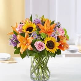 Mixed bouquet of sunflowers, lilies, and pink roses in a glass vase