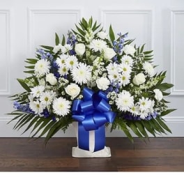 White and blue floral arrangement in a vase with a large blue ribbon
