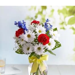 Bouquet of red, white, and blue flowers in a glass vase with a yellow ribbon